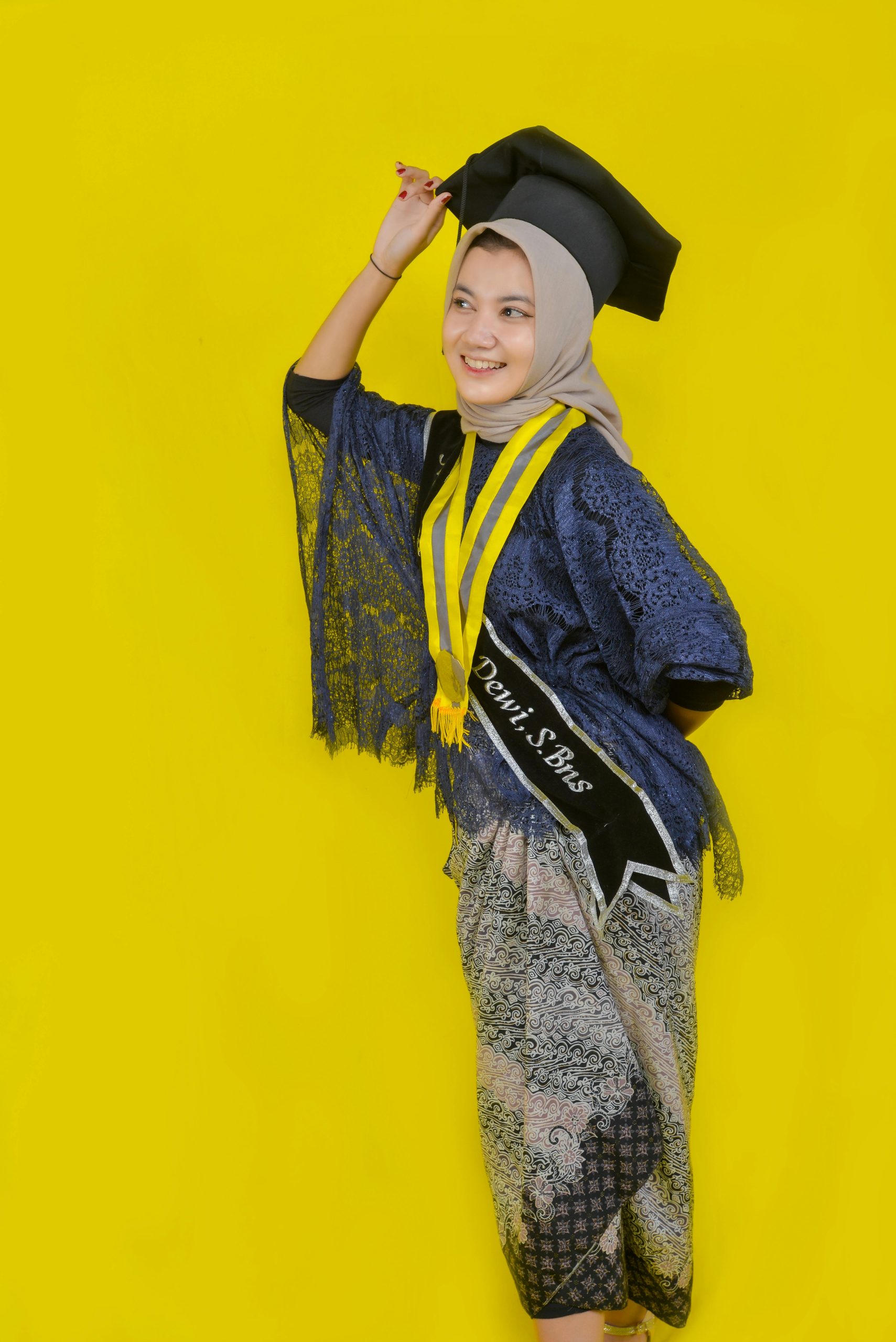 A young woman smiling in graduation attire against a vibrant yellow background.